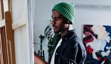 a young person in a green beanie painting at an easel