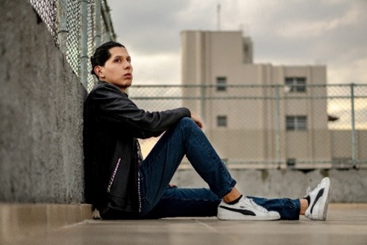 young person sitting outside against a cement wall