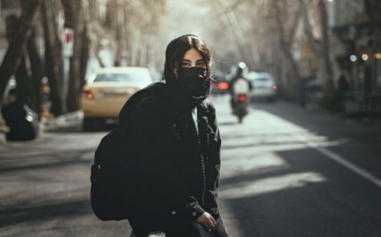 young person wearing a mask standing on a city street