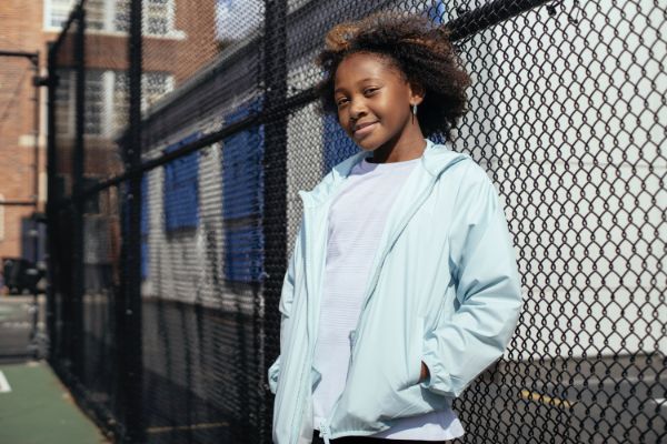 young Black girl standing in front of a fence on a playground